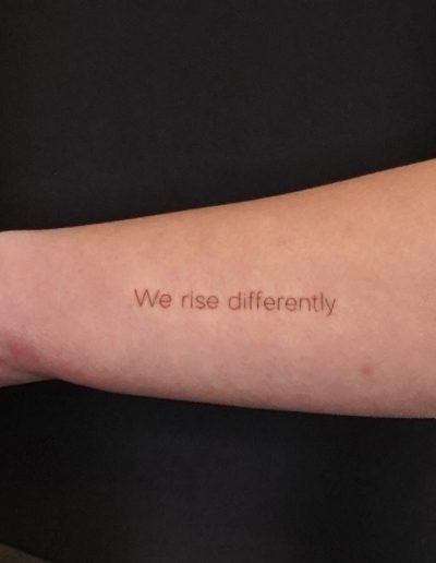 Tätowierter Schriftzug "we rise differently"